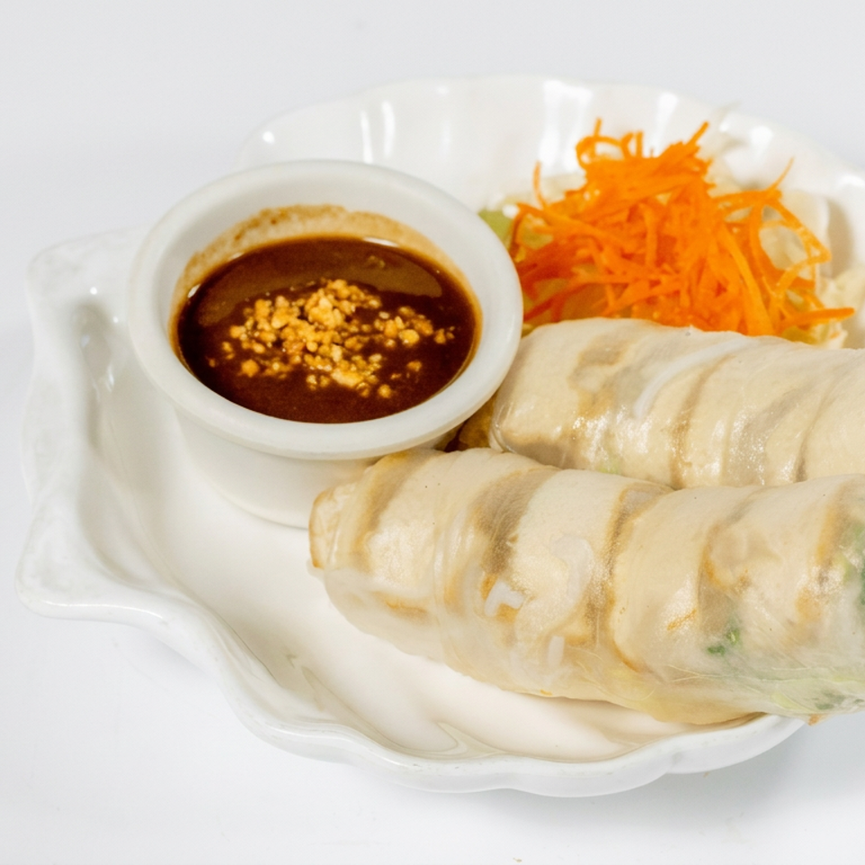 Two fresh Vietnamese spring rolls with shredded carrots and peanut dipping sauce on a white plate.