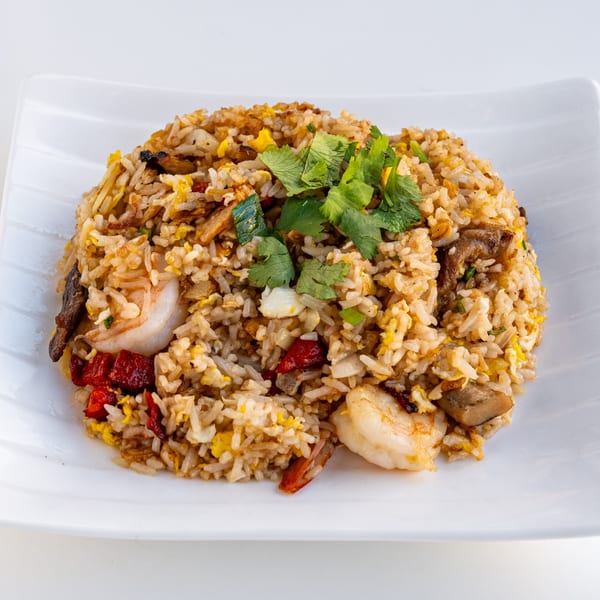 A white plate holds a mound of fried rice with shrimp, red peppers, and cilantro.