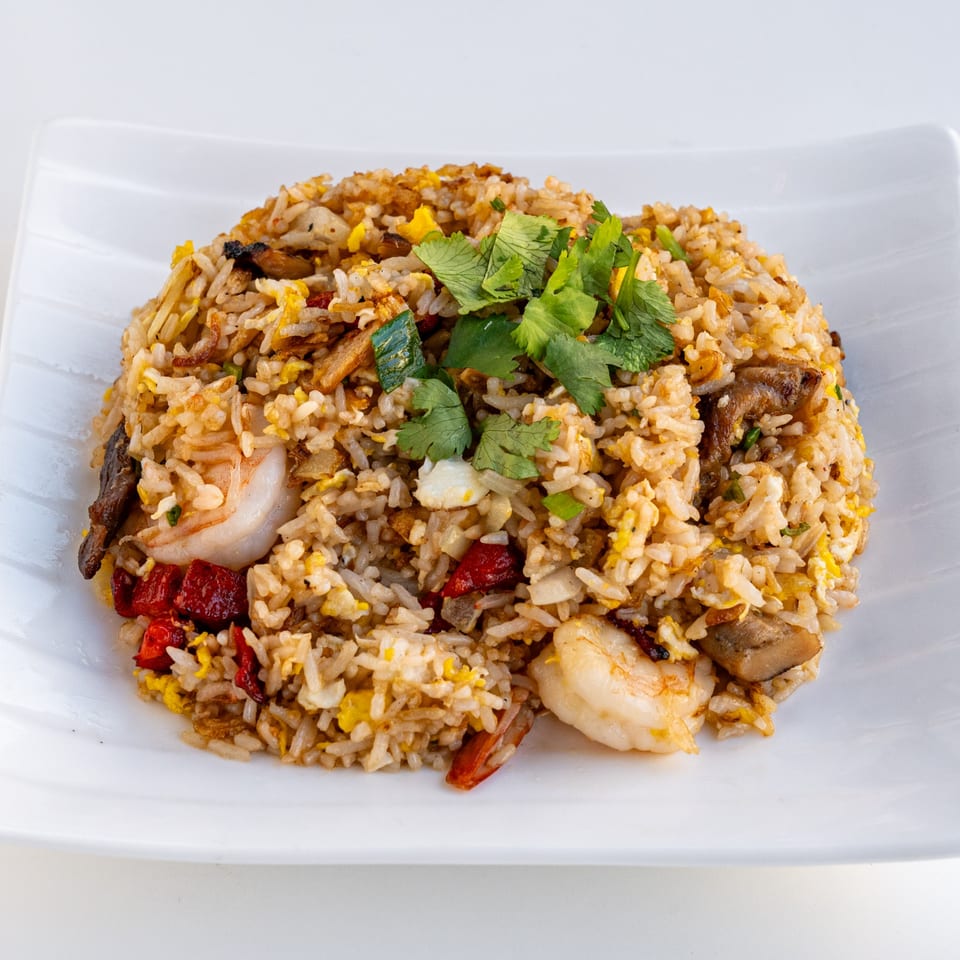 A white plate holds a mound of fried rice with shrimp, red peppers, and cilantro.