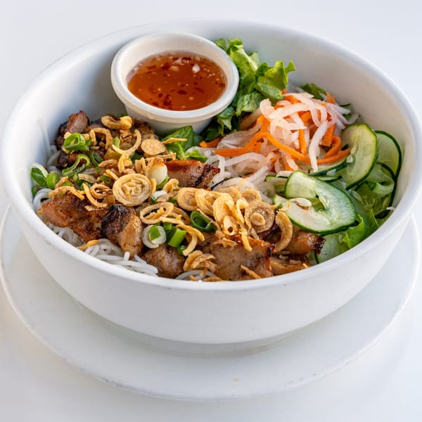 Vietnamese vermicelli bowl with grilled pork, fried onions, fresh vegetables, and dipping sauce.