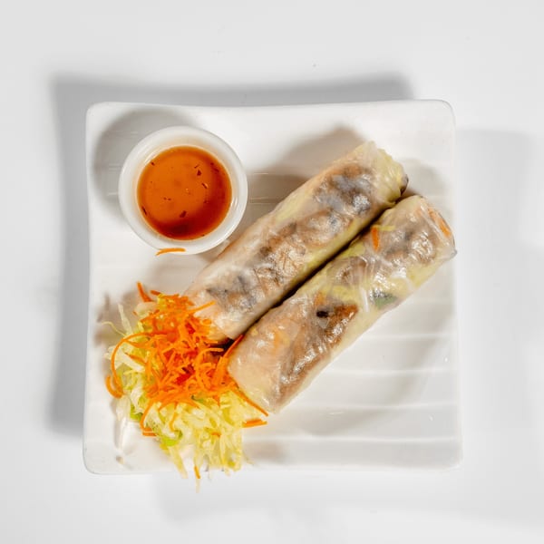 Two fresh spring rolls with shredded carrots and cabbage, served with a side of dipping sauce.