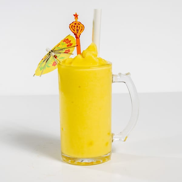 Bright yellow frozen drink in a glass mug with a small umbrella and star-shaped stirrer.
