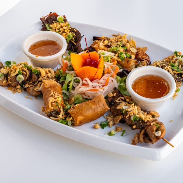 A white platter with various Vietnamese appetizers, including spring rolls, skewers, and dipping sauces.