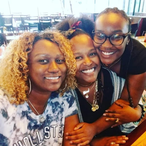 Three smiling women embracing each other at Pho 14, with restaurant tables and chairs in the background.