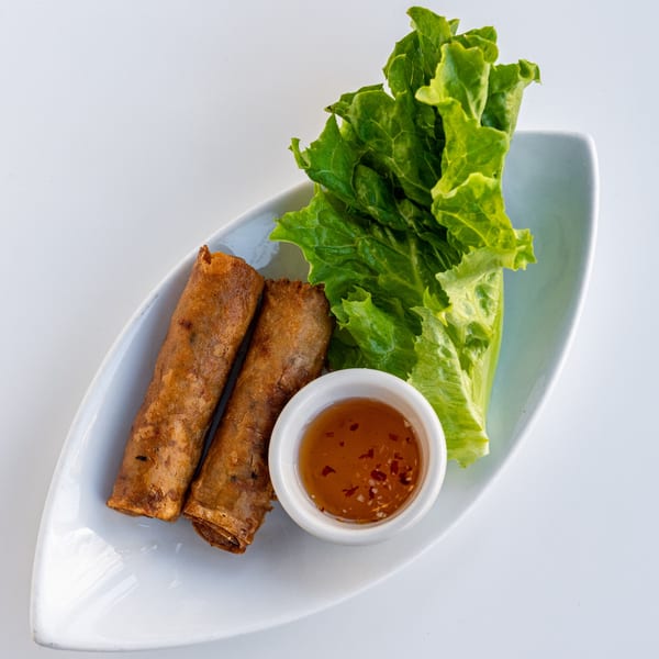 Two crispy spring rolls, fresh lettuce, and a small dish of chili dipping sauce on a white plate.