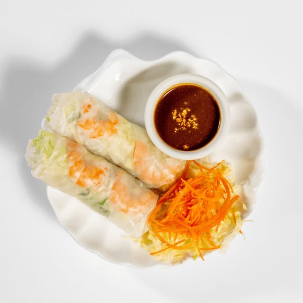 Two fresh spring rolls with shrimp and vegetables, served with peanut dipping sauce and shredded carrots.