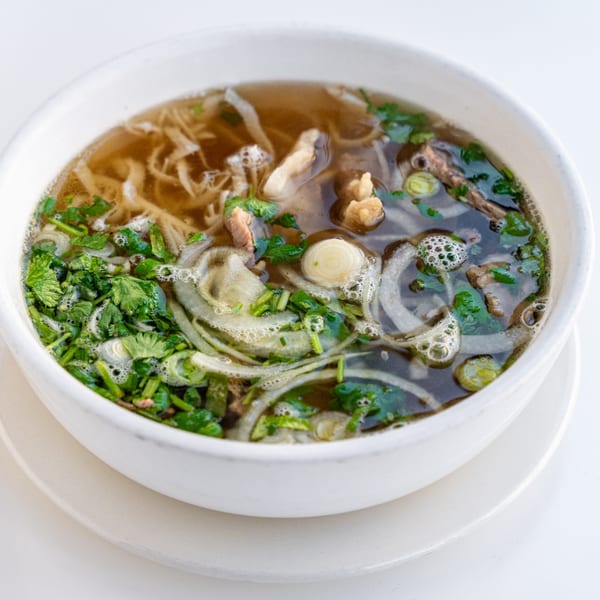 Close-up of a bowl of pho with broth, noodles, meat, onions, and fresh cilantro.