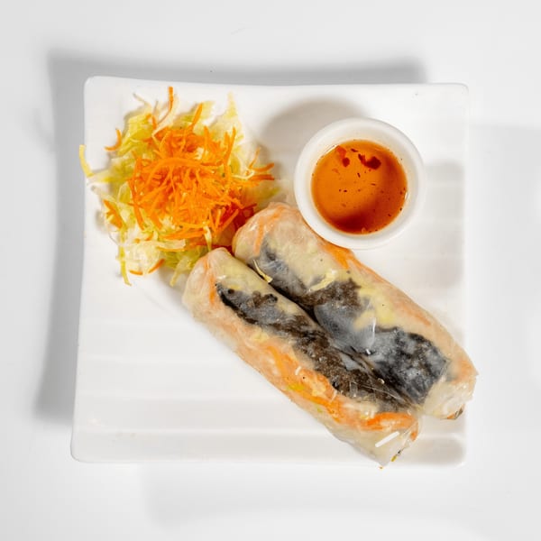 Two fresh spring rolls with shredded carrots and lettuce, served with a dipping sauce.
