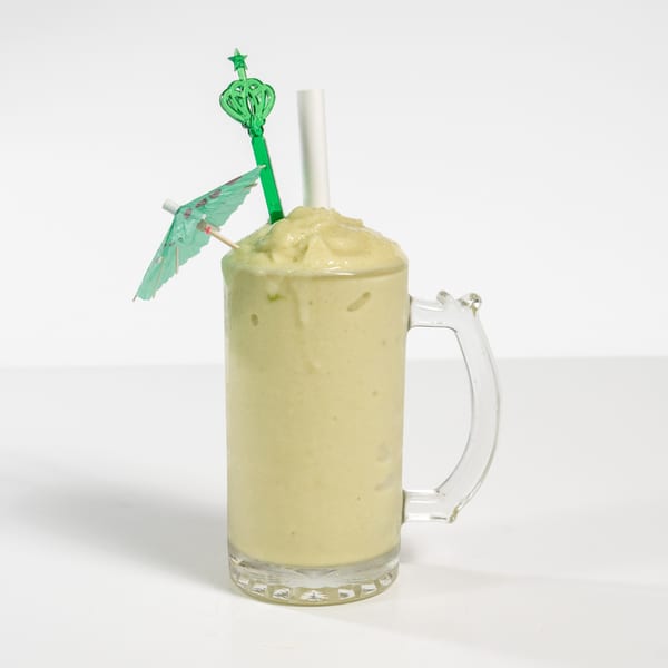 A green smoothie in a glass mug, garnished with a small green umbrella and a star-topped stirrer.