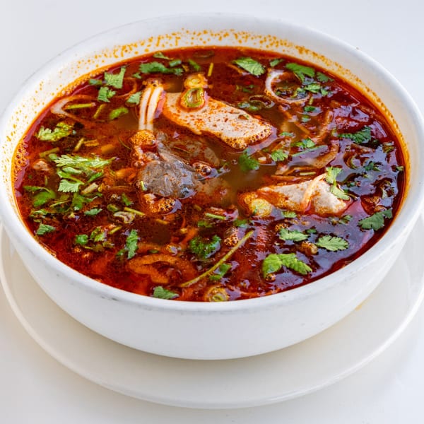 Close-up of a white bowl filled with a rich, red spicy soup, garnished with fresh cilantro.