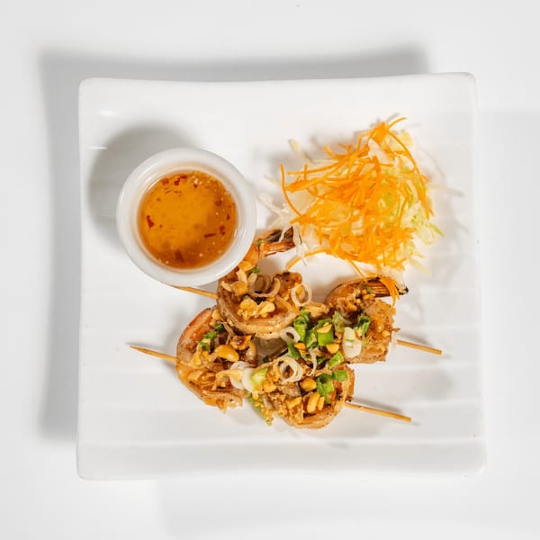 Shrimp skewers with peanuts, scallions, and fried shallots, served with sweet chili sauce and shredded carrots.