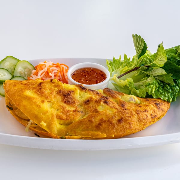 Golden Vietnamese bánh xèo crepe with pickled vegetables, fresh herbs, and dipping sauce.