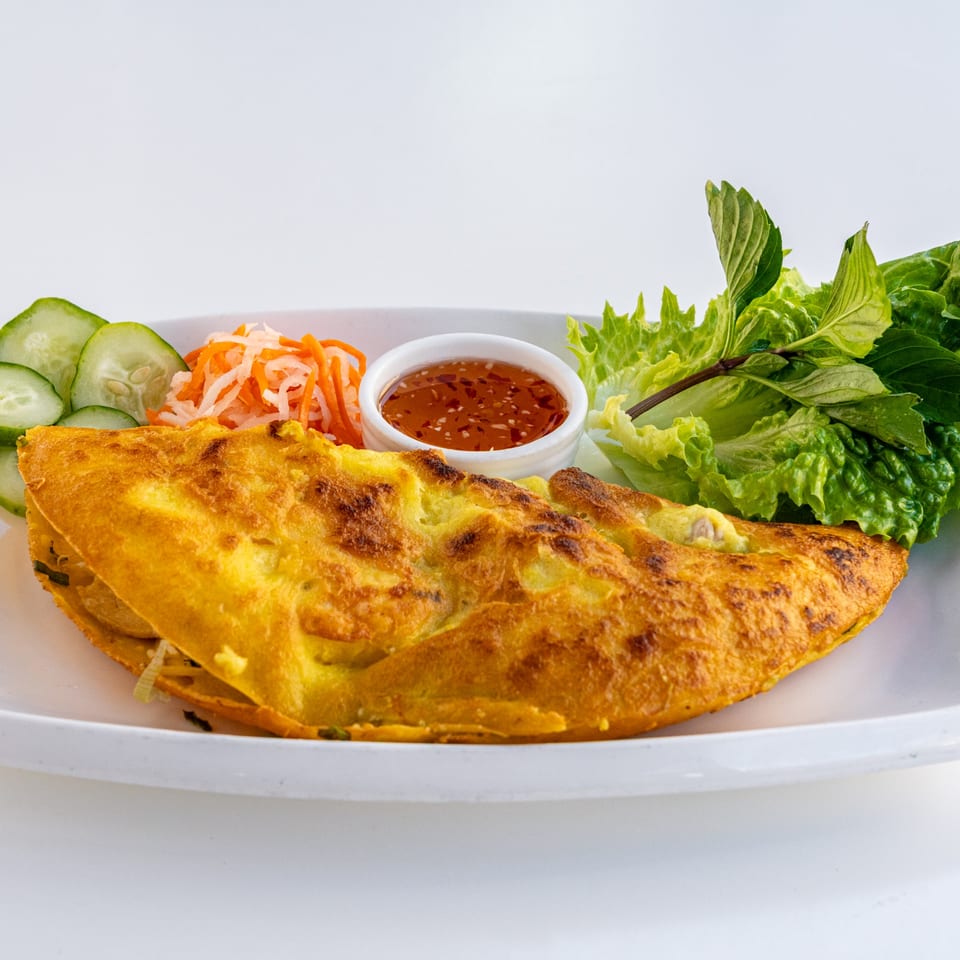 Golden Vietnamese bánh xèo crepe with pickled vegetables, fresh herbs, and dipping sauce.