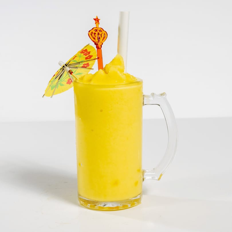 Bright yellow frozen drink in a glass mug with a paper umbrella and star-topped stirrer.