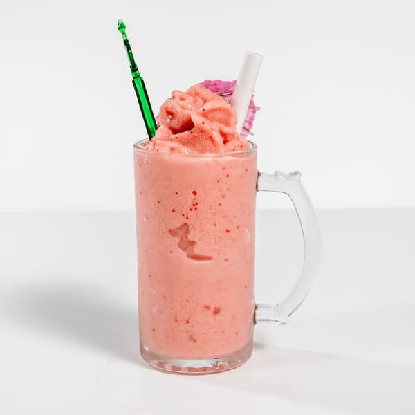 Pink strawberry smoothie in a glass mug with a green stirrer and a small pink umbrella.