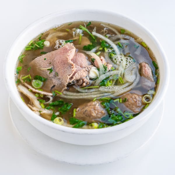 Close-up of a bowl of Vietnamese pho with beef, noodles, onions, and herbs in broth.